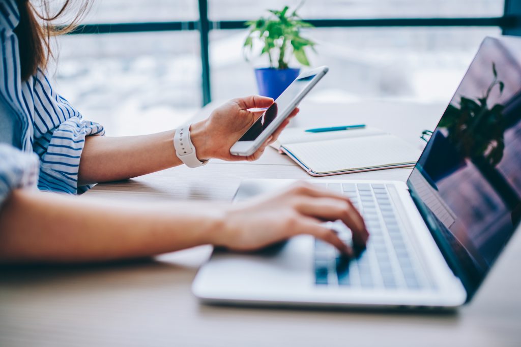 Cropped image of female holding smartphone getting message with confirmation making transaction on laptop computer,woman using mobile phone app for synchronizing data with netbook via bluetooth. Cropped image of female holding smartphone getting message with confirmation making transaction on laptop computer,woman using mobile phone app for synchronizing data with netbook via bluetooth